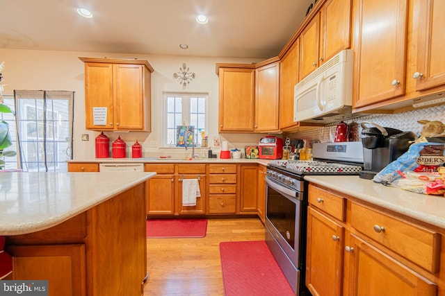 kitchen with tasteful backsplash, white appliances, sink, and light hardwood / wood-style flooring