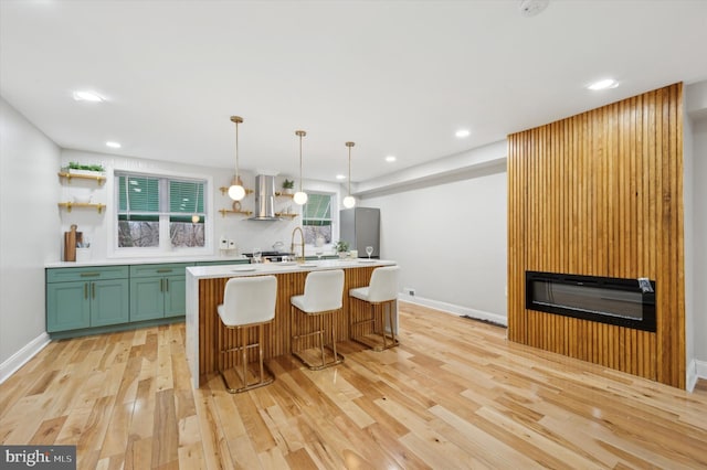 kitchen with pendant lighting, green cabinets, extractor fan, a center island with sink, and light wood-type flooring