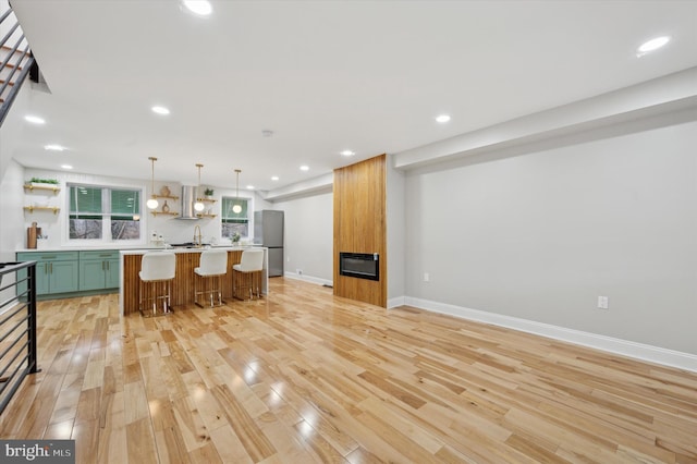 kitchen with stainless steel fridge, a breakfast bar, hanging light fixtures, exhaust hood, and light wood-type flooring