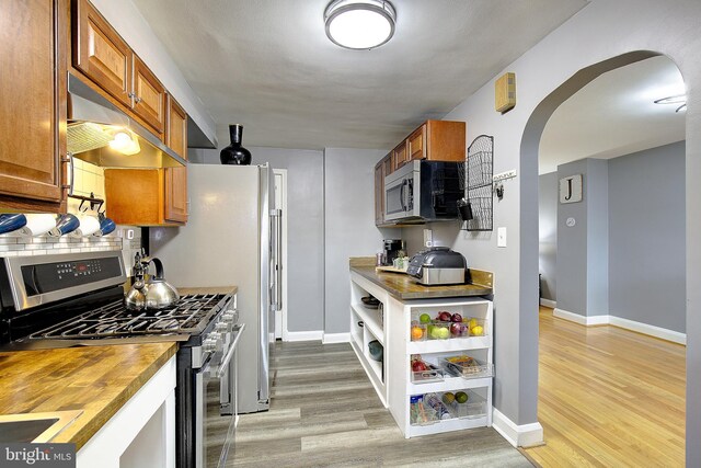 kitchen with backsplash, stainless steel appliances, wooden counters, and light wood-type flooring