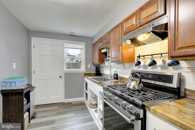 kitchen with backsplash, sink, gas stove, and light wood-type flooring