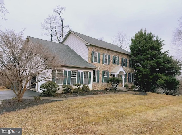 colonial-style house featuring a front yard and stone siding