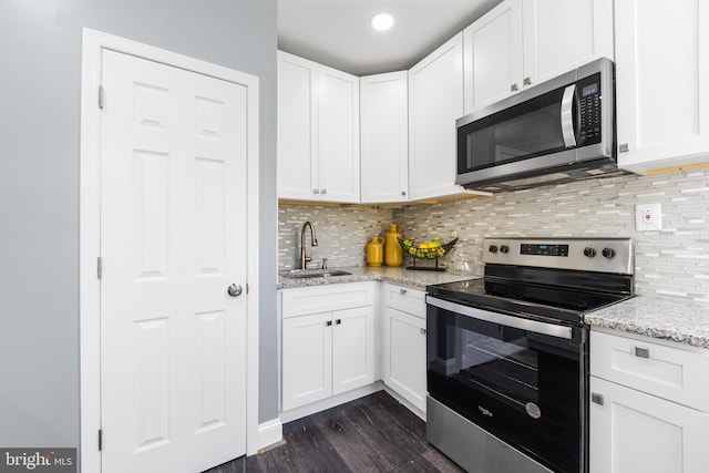 kitchen with sink, appliances with stainless steel finishes, light stone counters, white cabinets, and dark hardwood / wood-style flooring