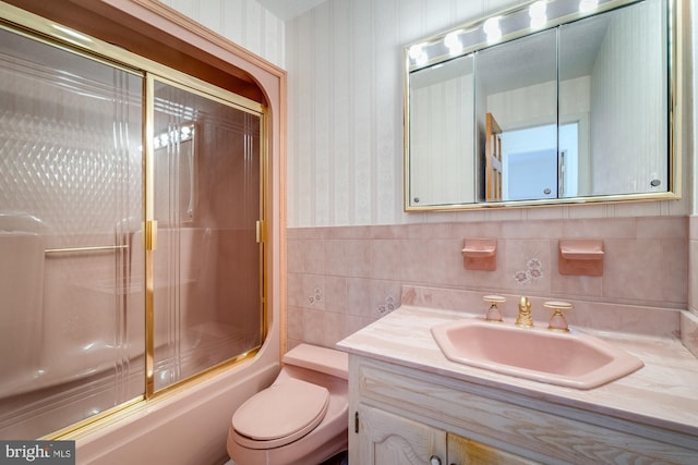 full bathroom featuring bath / shower combo with glass door, tile walls, vanity, and toilet