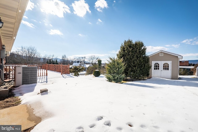 snowy yard with central AC unit and an outbuilding