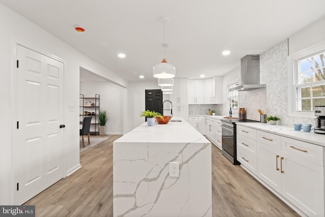 kitchen with stainless steel electric range oven, light wood-style flooring, backsplash, white cabinetry, and wall chimney range hood