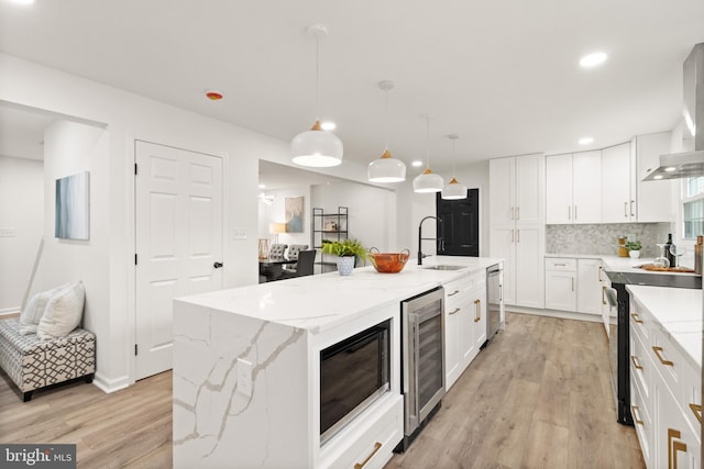 kitchen featuring beverage cooler, wall chimney exhaust hood, light wood-style flooring, stainless steel dishwasher, and a sink