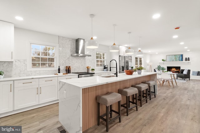 kitchen featuring light wood-type flooring, wall chimney range hood, a warm lit fireplace, and a sink