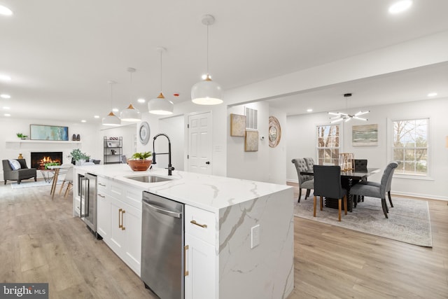 kitchen with stainless steel dishwasher, open floor plan, white cabinetry, a sink, and light wood-type flooring