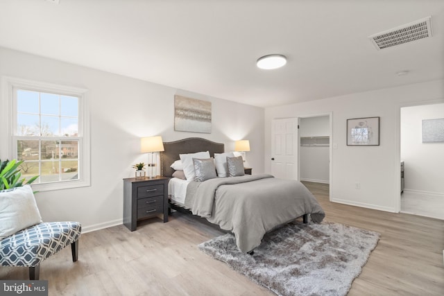 bedroom with a spacious closet, light wood-type flooring, visible vents, and baseboards