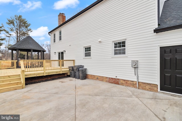 view of side of property featuring a deck, a patio, a gazebo, roof with shingles, and a chimney