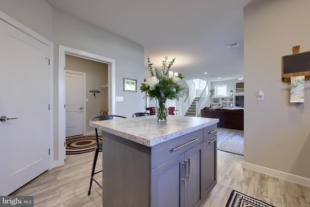 kitchen featuring gray cabinets, a kitchen island, a breakfast bar, and light wood-type flooring