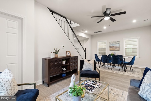 living room featuring light wood-style floors, visible vents, baseboards, and stairs