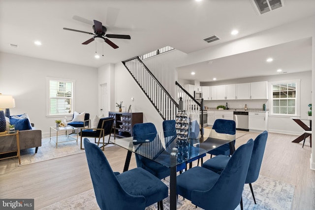 dining room featuring stairway, light wood-style flooring, visible vents, and baseboards