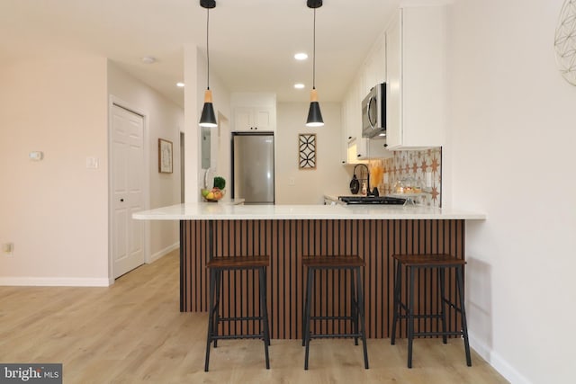 kitchen featuring white cabinetry, hanging light fixtures, appliances with stainless steel finishes, a kitchen breakfast bar, and kitchen peninsula