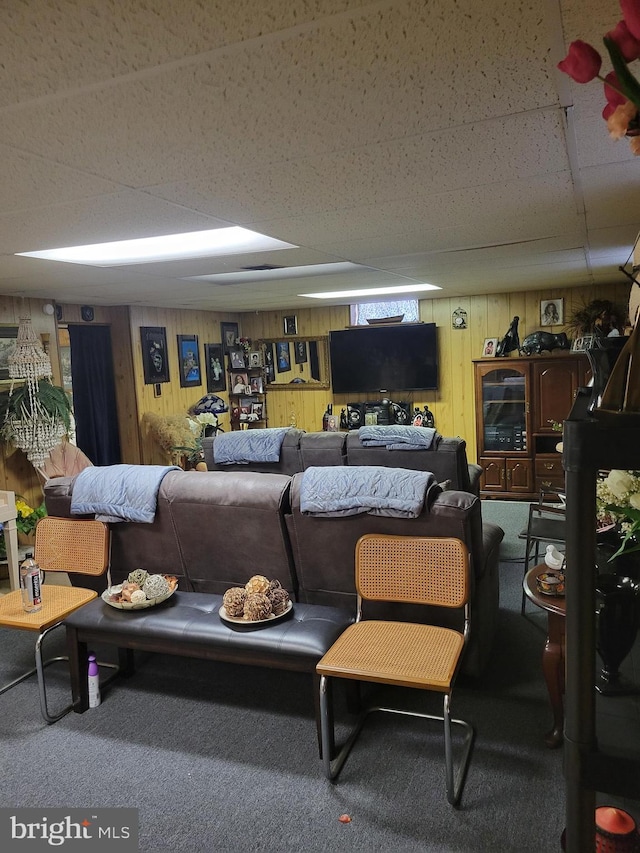 carpeted living room with a drop ceiling and wood walls