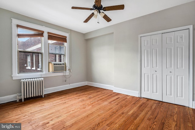 unfurnished bedroom featuring light wood-type flooring, radiator heating unit, a closet, cooling unit, and ceiling fan