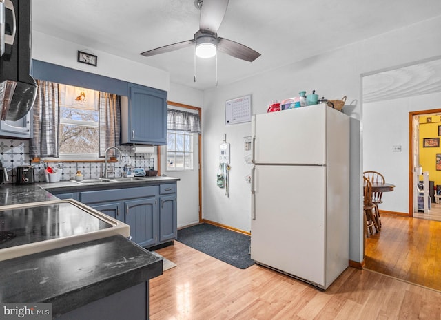 kitchen with blue cabinets, white fridge, sink, and light hardwood / wood-style flooring