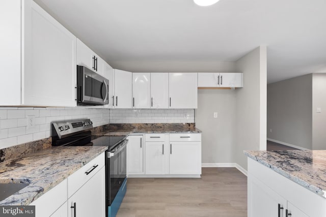 kitchen with tasteful backsplash, white cabinets, light stone counters, stainless steel appliances, and light wood-type flooring