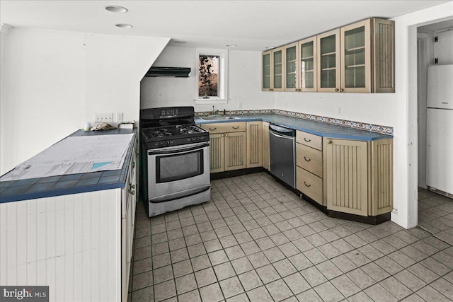 kitchen with a sink, glass insert cabinets, cream cabinets, and appliances with stainless steel finishes