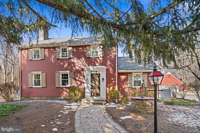 colonial inspired home featuring a chimney and roof with shingles