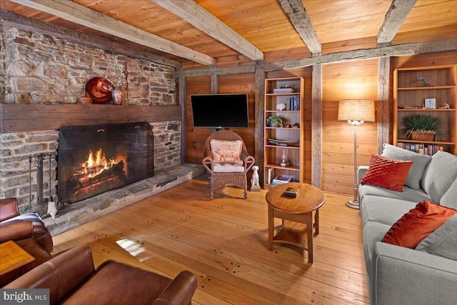 living room featuring a stone fireplace, beamed ceiling, wood finished floors, and wood ceiling