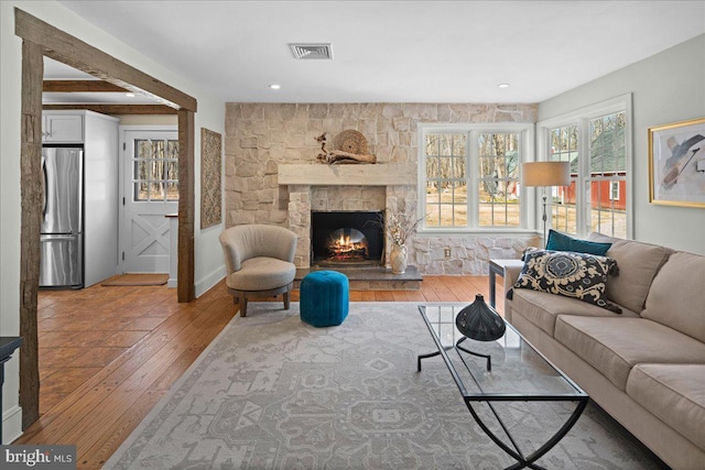 living area with a stone fireplace, light wood-type flooring, and visible vents