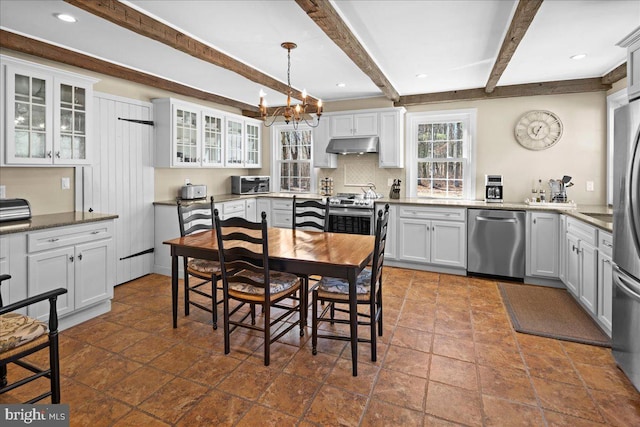 kitchen with under cabinet range hood, stainless steel appliances, white cabinetry, hanging light fixtures, and glass insert cabinets