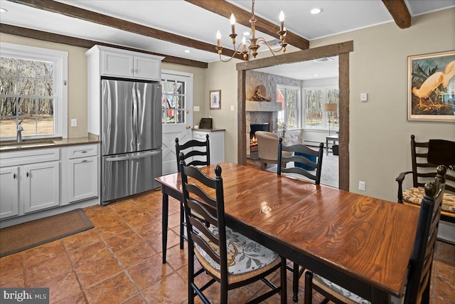 dining area featuring beamed ceiling, a fireplace, and an inviting chandelier