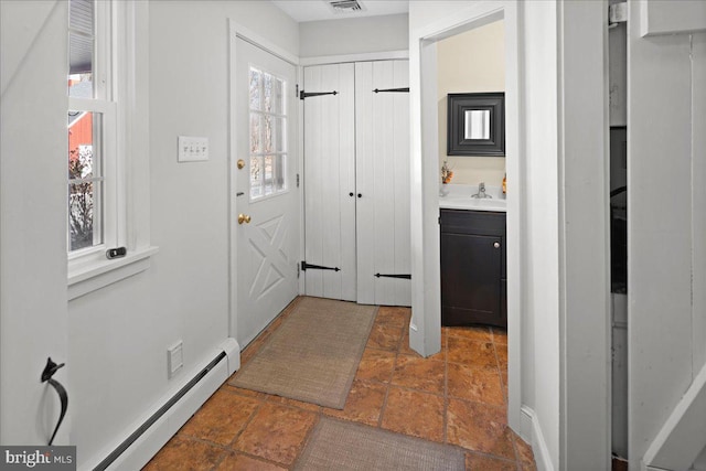 doorway featuring visible vents, a baseboard heating unit, a sink, and stone finish flooring