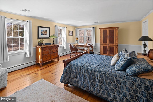 bedroom with a baseboard radiator, multiple windows, visible vents, and wood finished floors