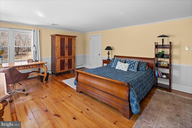 bedroom featuring a baseboard radiator, a wainscoted wall, visible vents, and wood finished floors