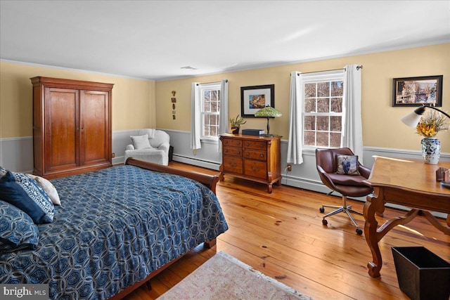 bedroom featuring a wainscoted wall, multiple windows, baseboard heating, and wood finished floors