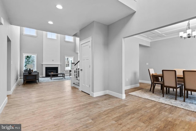 interior space with a notable chandelier, a towering ceiling, a fireplace, and light wood-type flooring