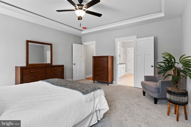 carpeted bedroom featuring ensuite bathroom, ceiling fan, and a tray ceiling