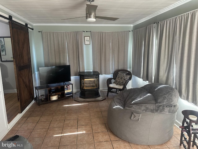 living room with a barn door, a ceiling fan, ornamental molding, a wood stove, and tile patterned flooring