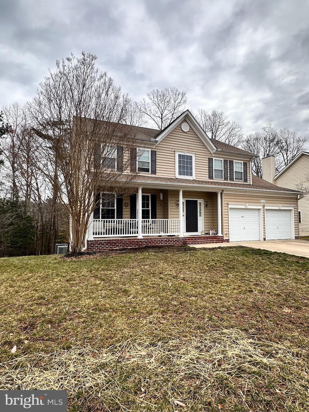 traditional-style home with covered porch, driveway, a front lawn, and a garage