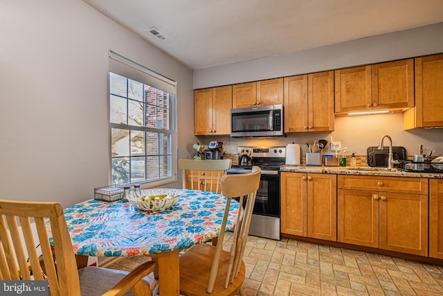 kitchen featuring stainless steel appliances, light stone countertops, and sink