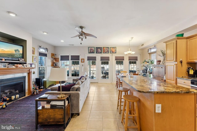 tiled living room featuring ceiling fan with notable chandelier and a tile fireplace