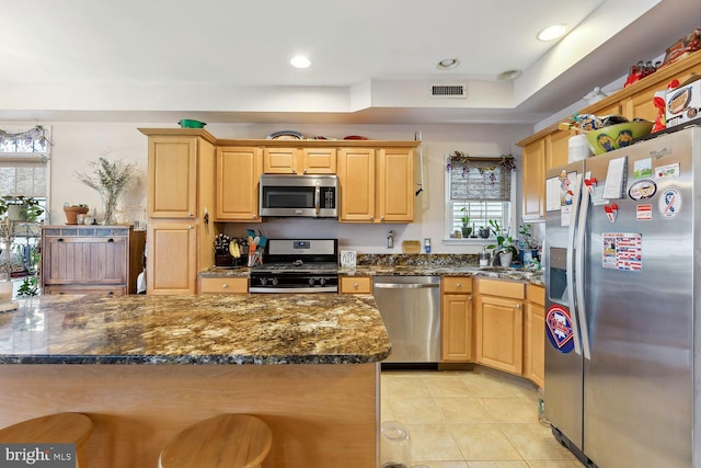 kitchen featuring dark stone countertops, appliances with stainless steel finishes, light tile patterned floors, and light brown cabinets