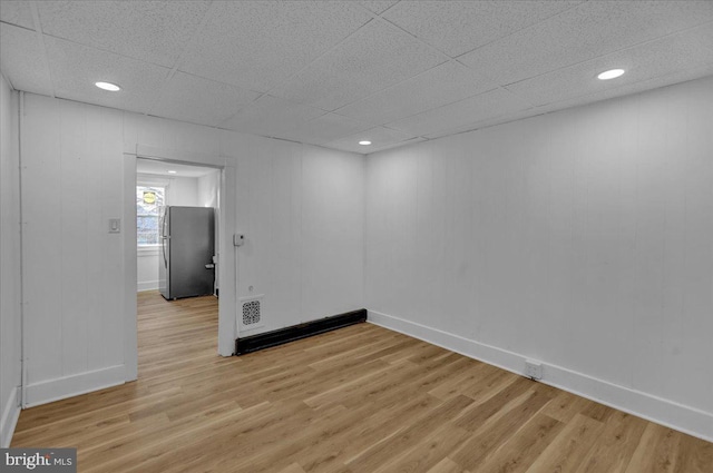 empty room with a drop ceiling and light hardwood / wood-style flooring