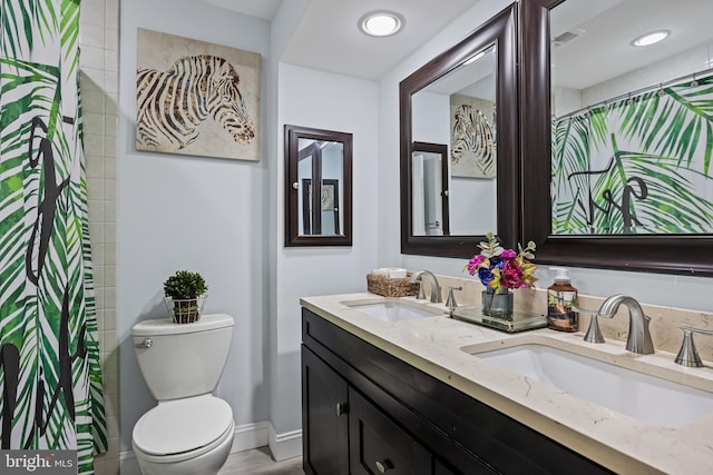 full bathroom featuring double vanity, a sink, toilet, and baseboards