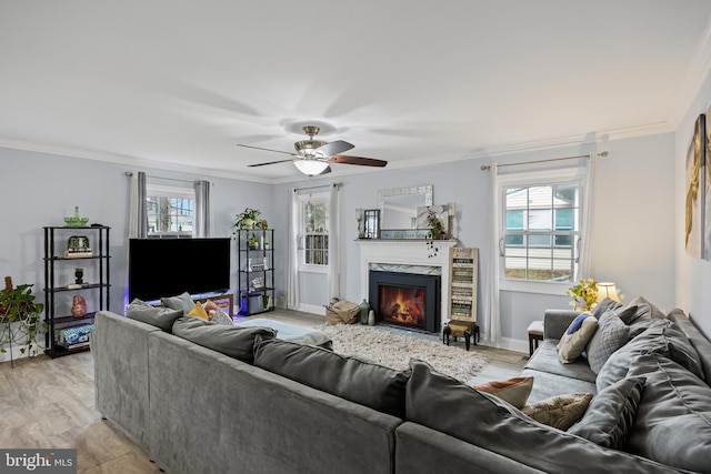 living area with baseboards, light wood-style flooring, a premium fireplace, ceiling fan, and crown molding