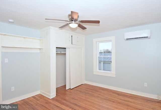 unfurnished bedroom with a wall mounted air conditioner, light hardwood / wood-style flooring, a closet, and ceiling fan