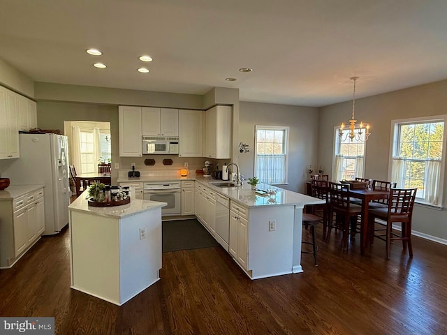 kitchen featuring sink, white appliances, white cabinets, decorative light fixtures, and kitchen peninsula