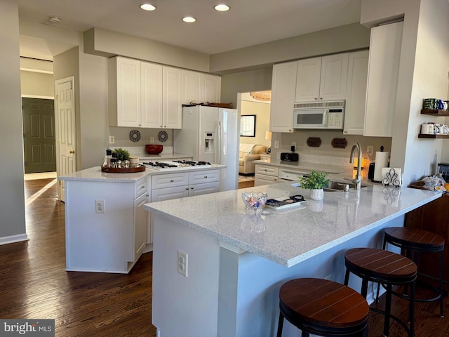 kitchen featuring white cabinetry, sink, kitchen peninsula, light stone countertops, and white appliances