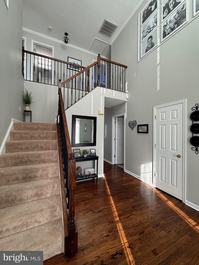 staircase with crown molding, a towering ceiling, and hardwood / wood-style floors