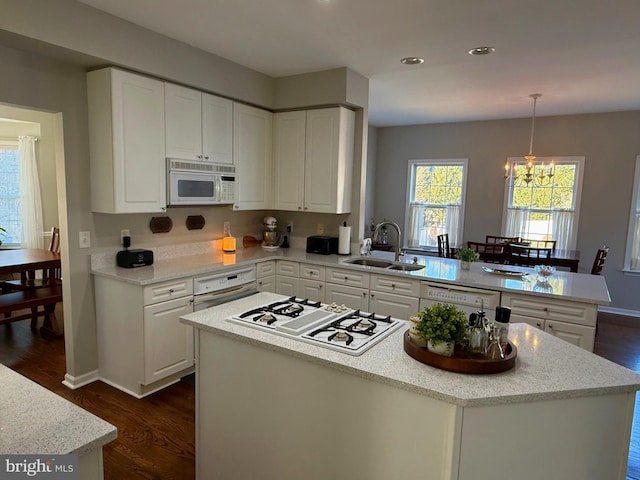 kitchen with sink, white cabinetry, hanging light fixtures, kitchen peninsula, and white appliances