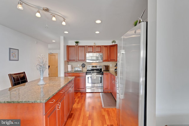 kitchen with light stone counters, a center island, light wood-type flooring, a kitchen breakfast bar, and stainless steel appliances