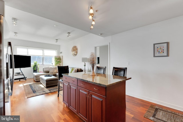 kitchen with hardwood / wood-style floors, light stone countertops, a kitchen island, and a breakfast bar area